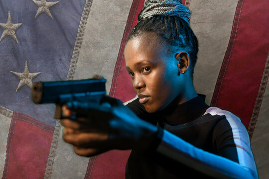 Hollywood movie style portrait of young attractive and confident black African American woman holding gun as special federal agent isolated in USA flag background
