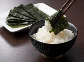 Wrapping nori around rice set against a wooden backdrop. - obrazy, fototapety, plakaty