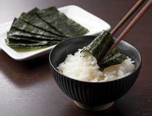Wrapping nori around rice set against a wooden backdrop. - obrazy, fototapety, plakaty
