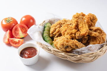 Crispy fried chicken on wicker basket  serve with cucumber and  ketchup on white background 
