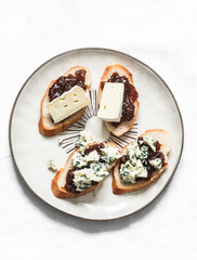 Crostini with fig jam, gorgonzola and brie cheese  on a light background, top view