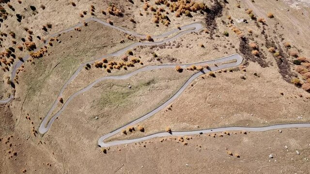 Road to the Gavia mountain pass in Italy. Up and down amazing aerial view of the mountain bends creating beautiful shapes. Fall time. Warm colors. Nobody on the road