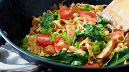 Stir fried noodles with turkey meat and fresh spinach and vegetables in an iron wok pan. Chinese cuisine.