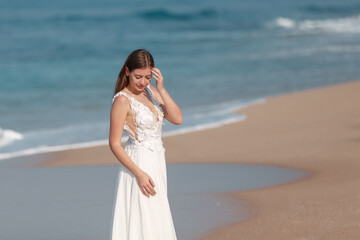 Fototapeta na wymiar Portrait of beautiful bride standing by the beach, toch her hair and looking down