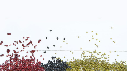 close up of red beans with black beans and green beans on white wooden background