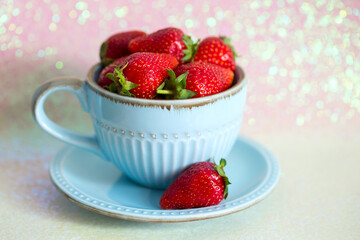 Sweet strawberries in a light blue ceramic Cup and saucer on a shiny background, stock food image, side view