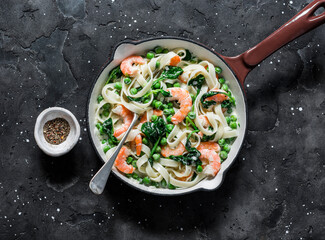 Green peas, prawns, spinach, cream sauce tagliatelle pasta in a cooking skillet  on a dark background, top view