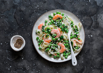 Green peas, shrimps, spinach, cream sauce tagliatelle pasta  on a dark background, top view. Mediterranean food style
