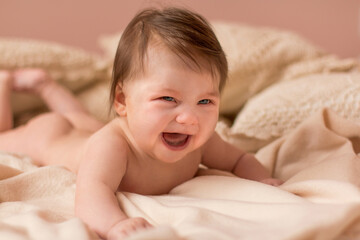 Portrait of adorable smiling newborn baby with thick brown hair . Nude newborn child relaxing in bed.