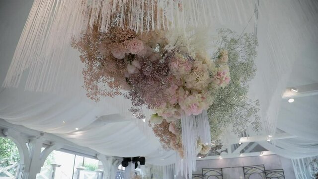 Expensive luxury decor in the interior decorated with fresh blooming flowers of peonies, baby's breath gypsophila, roses. Ceiling chandelier decorations for an event. White pink colors.
