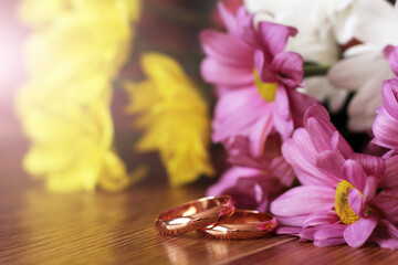 Closeup of wedding rings and color flowers on wooden table