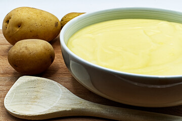Bowl of mashed potatoes puree, with raw potatoes. Closeup