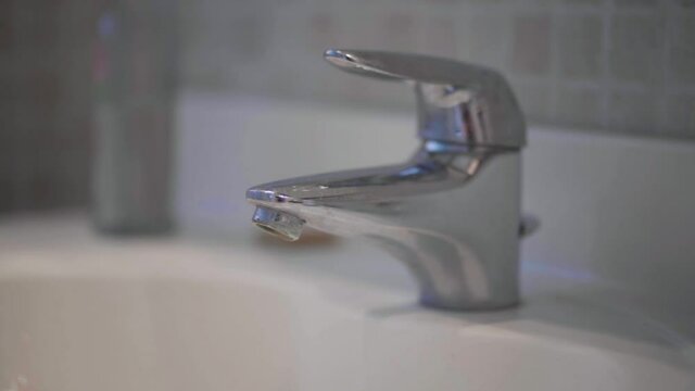 A faulty silver chrome bathroom faucet slowly dripping water, wasting precious resources