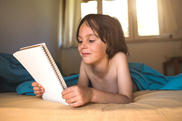 The boy lies in bed and reads a book.