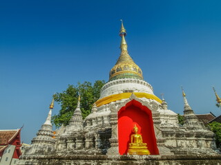 Fototapeta premium view of yellow Seated Buddha in arch flame with white pagoda lanna style art and blue sky background, Wat Buppharam in Chiang Mai City, northern of Thailand.