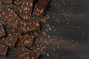 Fototapeta na wymiar Grated chocolate with choco bars on dark background, flat lay.