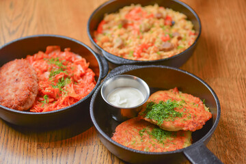 Delicious potato pancakes with sour cream, rice with meat and vegetables and Chicken Kiev cutlet served in frying pans.