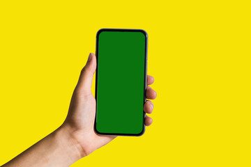 Hand holding white mobile phone with blank green screen in Yellow background.