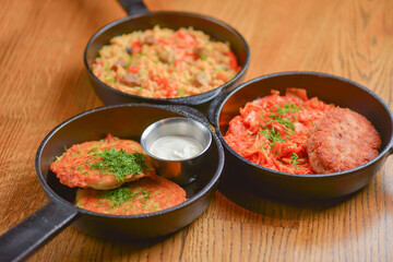Delicious potato pancakes with sour cream, rice with meat and vegetables and Chicken Kiev cutlet served in frying pans.