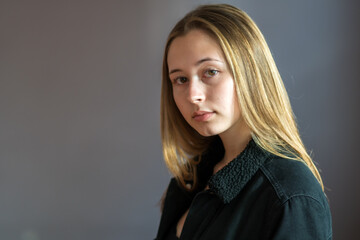 Fototapeta premium Semi profile portrait of a pretty teenage girl with long natural blonde hair and smooth skin looking at the camera. Studio shot