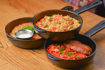 Delicious potato pancakes with sour cream, rice with meat and vegetables and Chicken Kiev cutlet served in frying pans.