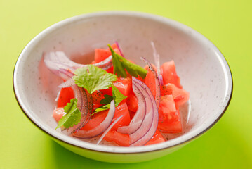 Fresh salad with red onion, tomatoes and basil. Served in a white bowl over bright green background.