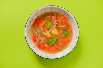 Delicious stew soup with meat and vegetables served in a white bowl over bright green background. Healthy diet.