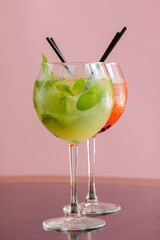 Two mojito alcohol cocktails with plastic straw, tropical beverage with ice, mint and lime on pink background copy space