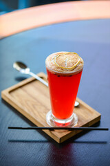 Mary Pickford cocktail, red coctail with foam in a tall glass on the table. Blurred background.