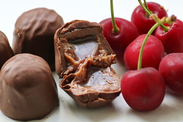 chocolate candies with starchy corn syrup and condensed milk on a white plate with ripe, puff, juicy sweet cherry berries close-up, macro