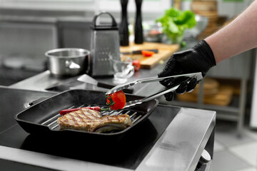Close-up of a chef's hand holding a grill pan with grilled steaks and vegetables