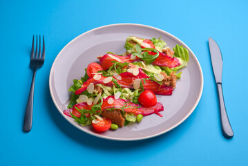 Fresh salad with smoked salted salmon, tomatoes and pumpkin seeds. Served on a gray plate over gray texture background.