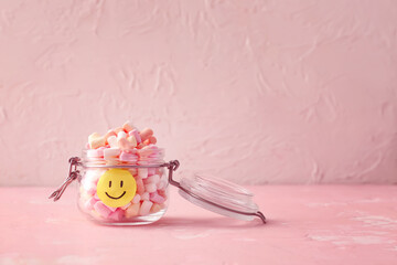 Jar with tasty marshmallows and paper smile on color background