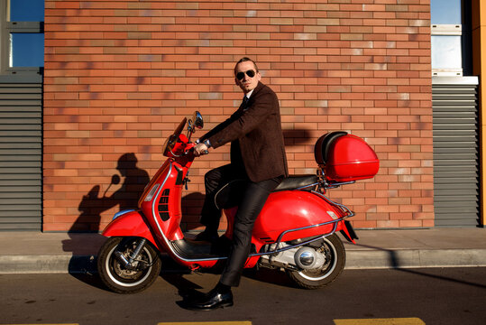 Street photo concept of a young elegant man in classic suit on a red vintage motorbike scooter