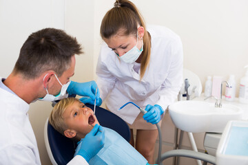 Stomatologist man with woman assistant are diagnosticating to young patient which is sitting