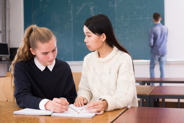 Girl student helping Chinese girl schoolmate prepare for exam