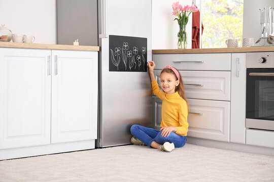 Little Girl Drawing On Chalkboard In Kitchen