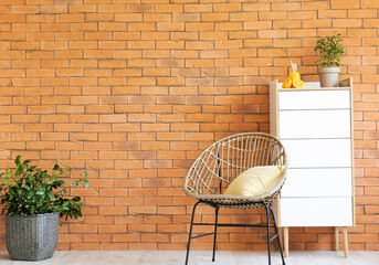 Stylish armchair with chest of drawers near brick wall in living room