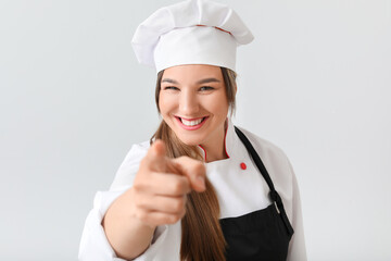 Young female chef pointing at viewer on light background