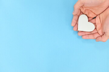 Cupped hands holding a white heart in blue background. Charity, pure love, compassion and kindness...