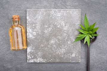 Cannabis cbd essential oil bottle and green leaves on gray flat lay background with copy space.