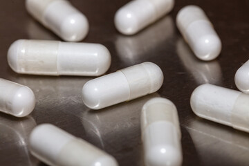 White pills scattered on scratched metal surface. Majority of the pills and much of the surface are in soft focus. Angled / close-up shot. Healthcare / hospital concept.