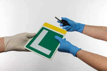 Spanish driver school teacher giving learner green driver sign, a student holding car key, using protective gloves for covid-19 pandemic prevention  