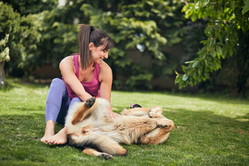 Young attractive fit yogi brunette playing with her dog in backyard.
