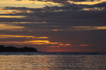 Sun behind clouds with exotic island silhouette