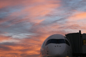 Fototapeta na wymiar Verkehrsflugzeug von vorne mit sonnenaufgang im Hintergrund rot gefärbte wolken am Flughafen