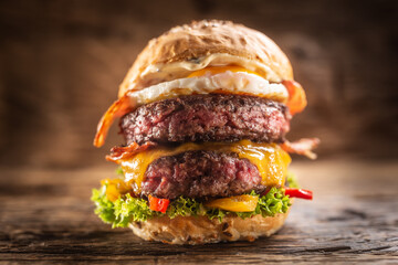 Detail of a massive double beef burger with fried egg, cheese, bacon, salad and peppers