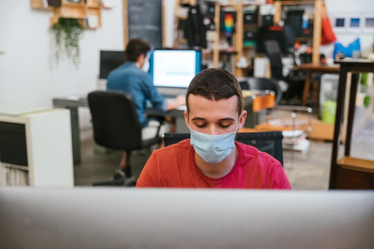 Millennials men with surgical mask at working at computer in office at distance for protection and prevention from Coronavirus, Covid-19