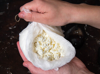 Fresh homemade cottage cheese in cheesecloth in women's hands