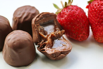 chocolate candies with starchy corn syrup and condensed milk on a white plate with ripe, puff, juicy sweet strawberry close-up, macro